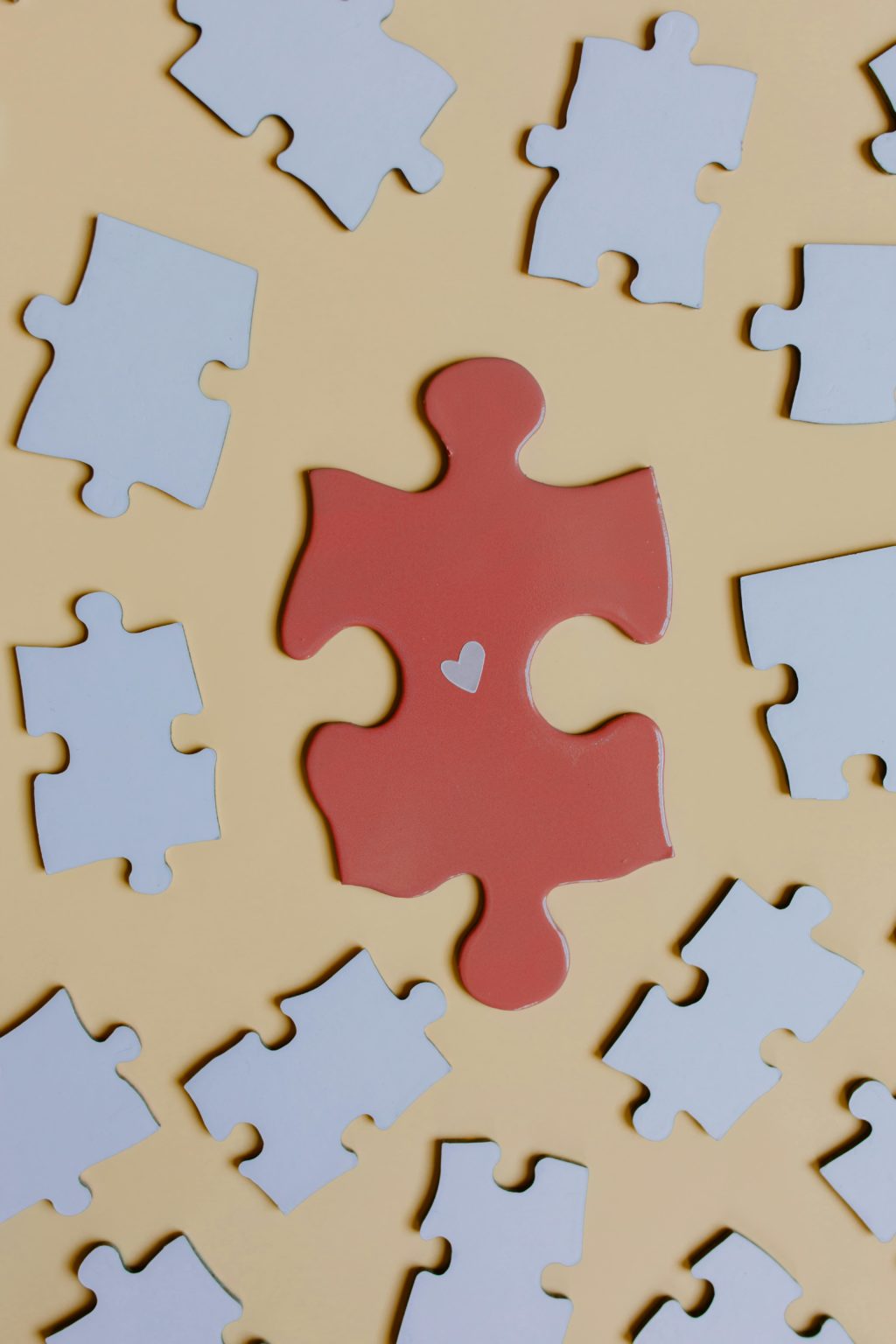 A red puzzle piece with a heart on a yellow surface surrounded by white puzzle pieces.
